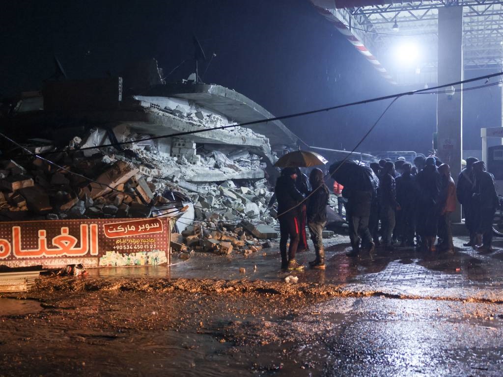 Residents gather in front of the rubble of a build